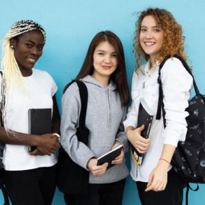 Three diverse young women with backpacks and books smiling against a blue background.